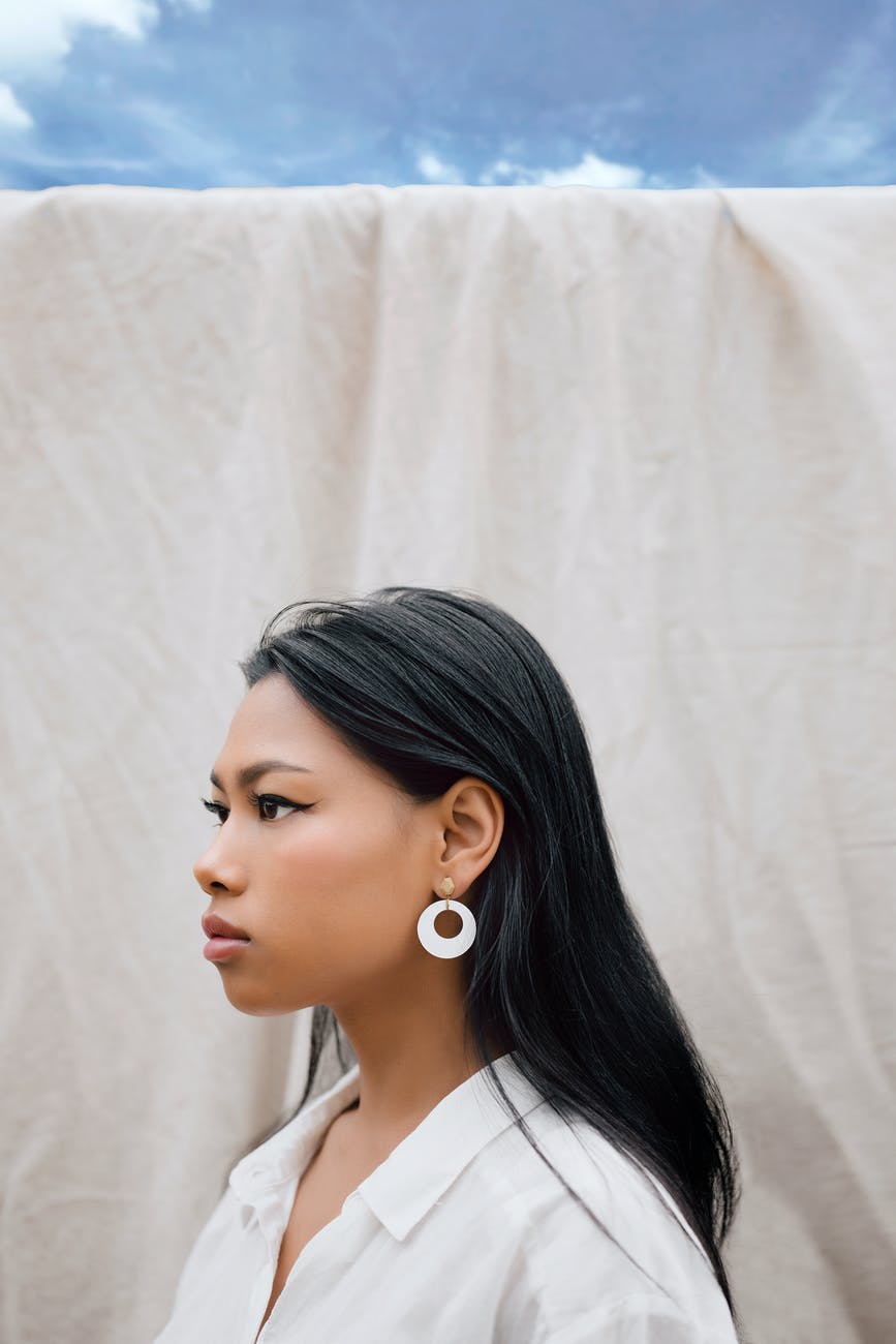 stylish young ethnic woman standing near white sheet against blue sky