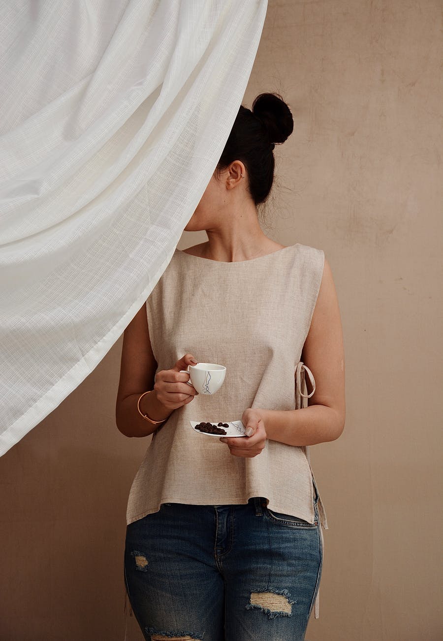 anonymous stylish woman with cup of coffee behind fabric